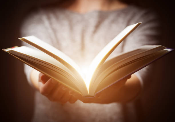 Close-up of hands holding an open book near a window